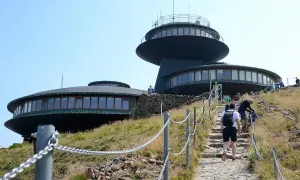 Wanderer steigen die Steintreppe zur Schneekoppe Seilbahn hinauf. Die futuristischen Gebäude auf dem Gipfel sind schon zu sehen.