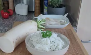 Ein frischer Rettich liegt neben einer Schüssel mit cremigem Rettichsalat, garniert mit Petersilie. Perfekt für ein leichtes Rettichsalat Rezept.