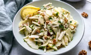 Ein frischer Staudensellerie Salat italienisch mit Äpfeln, Walnüssen und Kräutern, garniert mit einer Zitronenspalte.