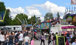 Buntes Treiben auf einem Volksfest mit Fahrgeschäften und vielen Besuchern. Ein Schiff-Karussell dreht sich, während Menschen an Ständen vorbeischlendern.