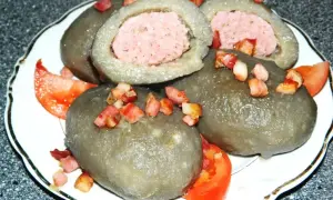Cepelin z mięsem, polany skwarkami i podany z pomidorem. Pyszne danie kuchni litewskiej.
