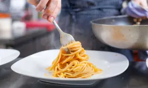 Eine Gabel hebt dampfende Spaghetti, ein Klassiker der Pasta italiana, auf einen weißen Teller.