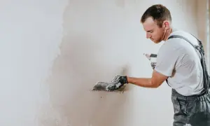 Operaio con spatola applica intonaco su muro. La rasatura è un passaggio cruciale per una finitura perfetta.