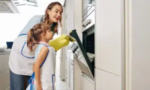 Mama i córka w fartuszkach otwierają piekarnik, by sprawdzić, czy trwa rozmrażanie w piekarniku.