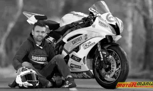 Czarno-białe zdjęcie motocyklisty Williama Dunlopa siedzącego obok swojego motocykla wyścigowego.