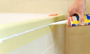 Dłoń nakłada silikon w łazience wzdłuż wanny, pokazując, jak nakładać silikon w łazience.