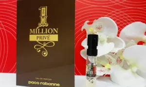 Złoty flakonik i próbka Paco Rabanne 1 Million Privé na tle czerwonych fal i białych kwiatów.