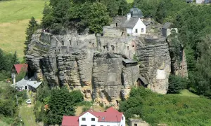Felsenburg Einsiedlerstein thront auf einem Sandsteinfelsen, umgeben von grünen Hügeln und Wäldern.