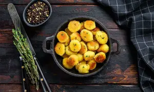 Crispy golden gnocchi in a black pan, garnished with herbs, on a wooden table with peppercorns and a knife.
