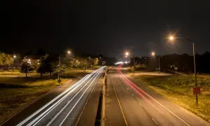 Luces de coches dejan estelas blancas y rojas en la carretera de noche, iluminada por el alumbrado de carretera.