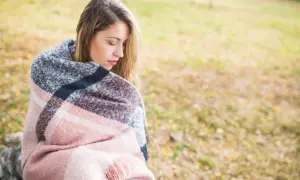 Młoda kobieta otulona kocem, zamyślona. Szuka sposobu, jak poradzic sobie z nadmiernym mysleniem.