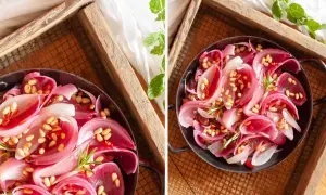 Cipolla rossa in agrodolce, guarnita con pinoli e rosmarino, servita in una ciotola scura su un vassoio di legno.