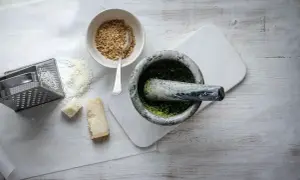 Mortel med grön pesto, riven parmesan, nötter och rivjärn. Ingredienser för ett klassiskt pesto recept.