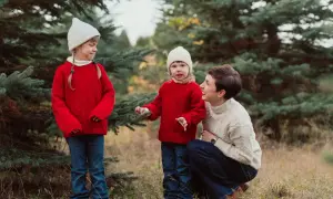 Urocza sesja zdjeciowa dzieci w świątecznych sweterkach i czapkach, wśród choinek.