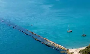 La spiaggia del Trave, con le sue acque turchesi, ospita due barche a vela e un piccolo motoscafo.