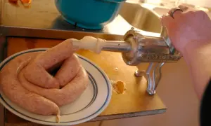 En hand vrider på en köttkvarn som gör korv. Ett korv-recept blir verklighet på tallriken.