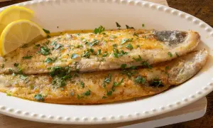 Delicioso lenguado a la plancha, dorado y jugoso, adornado con perejil fresco y rodajas de limón.