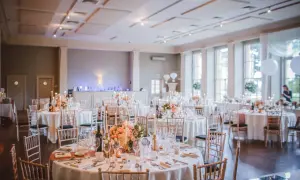 Elegancka sala imprez okolicznościowych przygotowana na przyjęcie. Okrągłe stoły nakryte białymi obrusami, ozdobione kwiatami i świecami.
