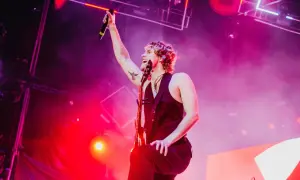 Luke Hemmings z 5 Seconds of Summer Polska na koncercie, z mikrofonem w dłoni i gitarą.