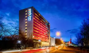 Wieczorna panorama miasta z oświetlonym budynkiem Park Inn Hotel Katowice i smugami świateł samochodów na drodze.