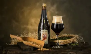 Una bottiglia e un bicchiere di birra Zahre, con chicchi d'orzo e luppolo, ingredienti per una birra artigianale di qualità.