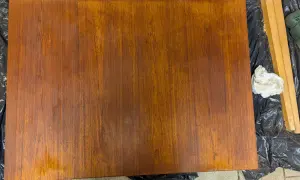 Förbereder för att slipa teak. En träyta ligger på svart plast, bredvid en slipmaskin och en trasa.
