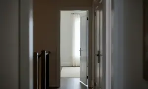 Korytarz z otwartymi drzwiami prowadzącymi do jasnego pokoju z zasłonami. Widoczny fragment balustrady schodów. 193 kk.