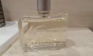 Szklana butelka perfum Lacoste Essential Sport z srebrną nakrętką, stojąca na blacie.