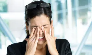Kobieta z zespołem Sjogrena, zamyka oczy i masuje nos, cierpiąc z powodu suchości i bólu.