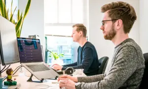 Deux développeurs travaillent sur leurs ordinateurs portables, plongés dans le code. Une scène typique d'une école de développeur moderne.