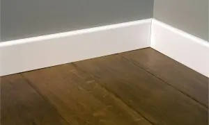 Esquina de una habitación con suelo de madera oscura y rodapiés blancos lisos, mostrando diferentes tipos de rodapiés.