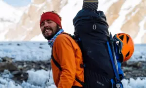 Kacper Tekieli, mit roter Mütze und orangefarbener Jacke, lächelt in die Kamera, bereit für sein nächstes Bergabenteuer.