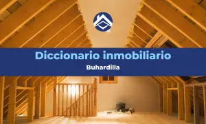 Interior de una buhardilla en construcción, con vigas de madera expuestas y una escalera. El texto indica "Diccionario inmobiliario: Buhardilla".
