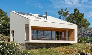 Casas de montaña modernas con paneles solares en el tejado, rodeadas de vegetación y rocas, con vistas a un paisaje montañoso.