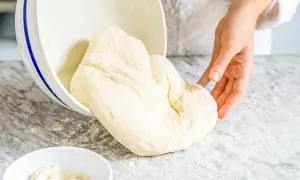 Frischer Pizzateig wird aus einer Schüssel auf eine bemehlte Arbeitsfläche gegeben. Das Mehl ist der Schlüssel für den perfekten Pizzaboden.
