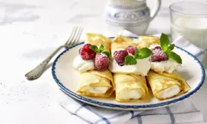Rolowane naleśniki z mascarpone, ozdobione malinami i miętą, wyglądają apetycznie. Idealne na deser!