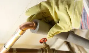 Hand mit Handschuh isoliert Kupferrohre, um Heizungsrohre zu verlegen und Energieverlust zu minimieren.