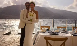 Un couple marié, maridat 19 63, pose près de la mer. La mariée tient un bouquet de callas. Une table de réception est dressée.