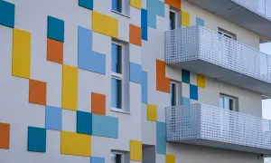 Nowoczesny budynek z kolorowymi, geometrycznymi panelami i białymi balkonami.