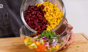 Kidneybohnen und Mais werden in eine Schüssel mit Paprika, Zwiebeln und Kräutern gegeben. Ein bunter Kidneybohnen Salat entsteht.