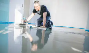 Mann kniet und beschichtet den Kellerboden mit einer Glättkelle. Der neue Boden glänzt spiegelnd.