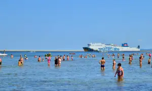 Ludzie kąpią się w morzu, a w tle płynie prom Polferries, który kursuje na trasie Świnoujście - Ystad.