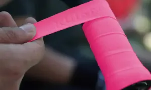 Mano applica nastro rosa su manubrio bici, mostrando la differenza tra grip e overgrip.