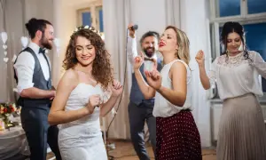 Brautpaar und Gäste tanzen ausgelassen. Frauen im lässigen Chic auf einer Hochzeit, die Braut trägt ein Spitzenkleid.