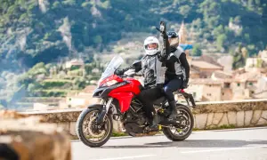 Para jadąca na czerwonym motocyklu Ducati, z pasażerem pozdrawiającym ręką.