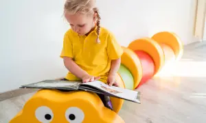 Małe dziecko w żółtej koszulce z zaciekawieniem czyta książkę, siedząc na żółtej gąsienicy.
