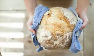 Mains d'une personne tenant un pain artisanal doré, tout juste sorti du four. Une belle réussite de recette pain.