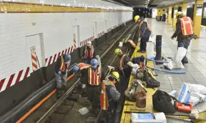 Des ouvriers en tenue de chantier, gilets de sécurité et casques, travaillent sur les voies d'une station de métro. Ils semblent engagés dans des travaux de maintenance, peut-être le prime habillage ou deshabillage de certains éléments.