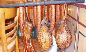 Wędzonki wiszą na drążku: kiełbasy, boczki i wędzonki w siatce. Idealne do marynaty do boczku.