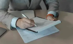 Rekruter w garniturze podpisuje dokumenty. Praca rekrutera to często analiza CV i rozmowy.